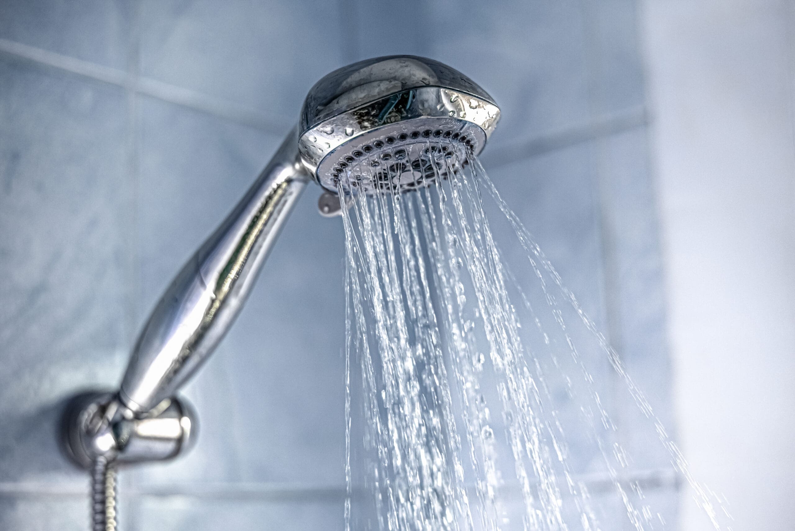 A silver showerhead spraying water in a bathroom, showcasing the artistry of bathroom installations. The water streams downwards against light blue tiled walls, creating a tranquil scene.
