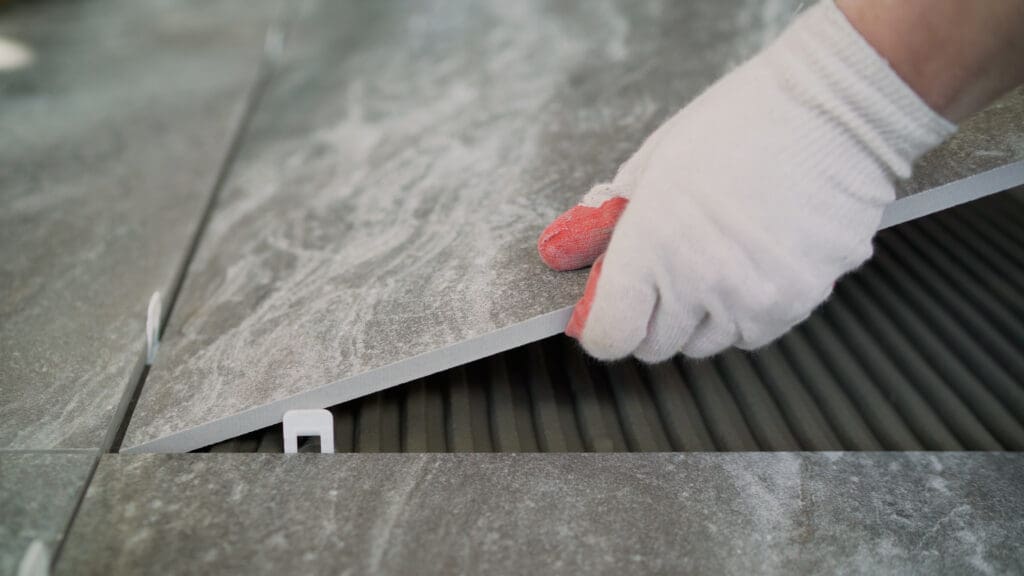 A worker puts a large tile on the floor. Workers are installing a large ceramic tile on the floor. Workers are laying the floor with large tiles.